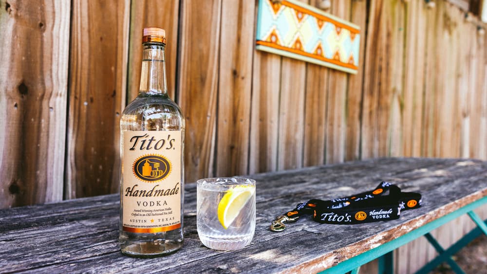 Tito's Watering Hole cocktail next to a Tito's Handmade Vodka Bottle and a Tito's dog leash