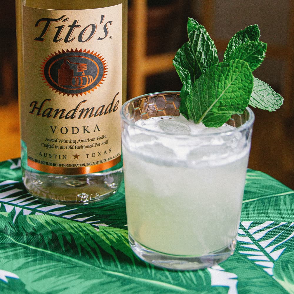 Tito's Motito cocktail garnished with a mint sprig next to a Tito's Vodka bottle