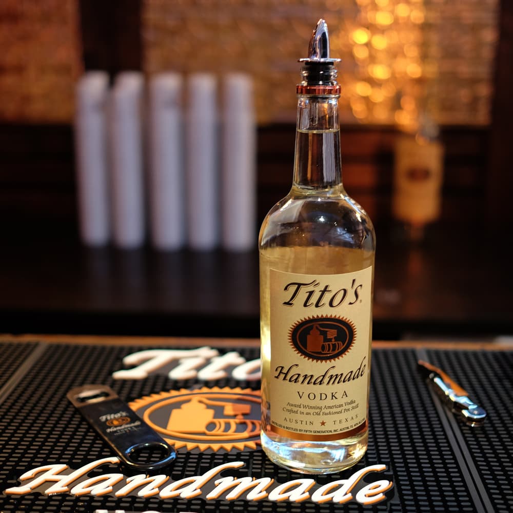 Tito's Vodka bottle on a bar top with Tito's bar mat and bottle openers