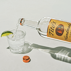 Tito's Handmade Vodka bottle pouring vodka into a glass with a lime wedge