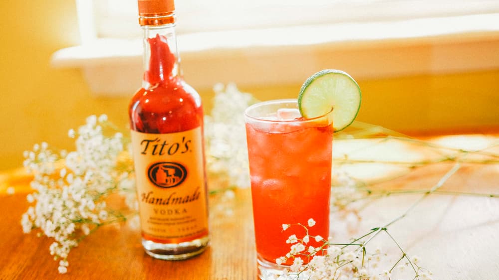 Tito's Vodka bottle filled with hibiscus flowers next to a Hibiscus Fizz cocktail garnished with a lime wheel