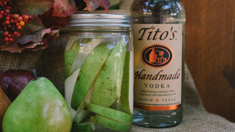 Tito's Vodka bottle next to mason jar with Tito's Pear Infusion inside