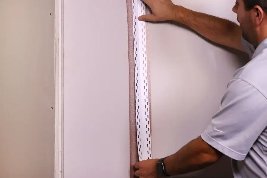 A person is holding up inside corner bead to a wall.