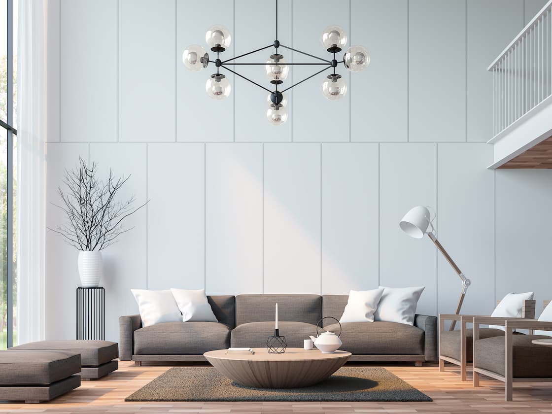 This living room area has a brown sofa, two chairs and two ottomans surrounding a round coffee table. There is a hanging light fixture in the room, along with white pillows on the furniture.