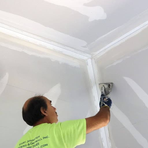 A person wearing a green shirt is applying drywall mud to a job site.