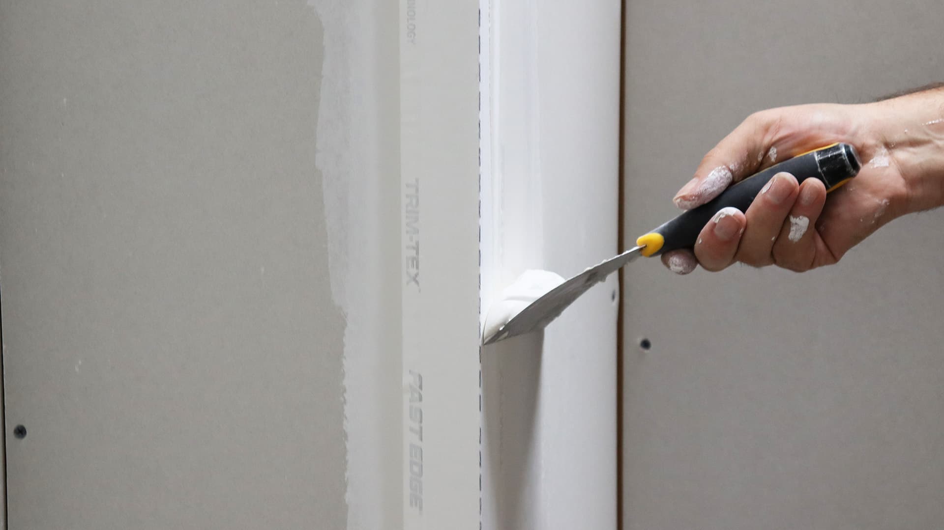 Fast Edge® Roll Is Thinner Than Other Rolled Corner Beads: a joint knife runs drywall mud up a rolled drywall corner bead