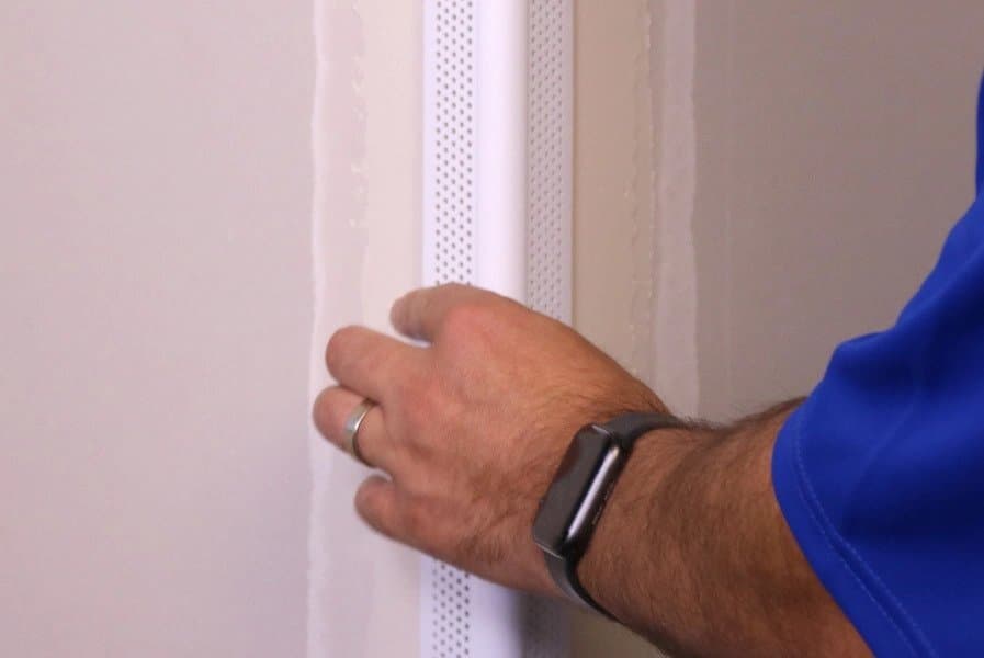 An image of a person’s hand placing corner beads onto the corner of a wall.