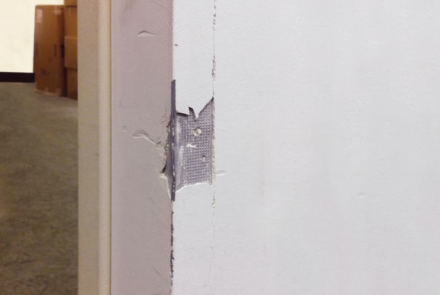 Metal corner bead is revealed below damaged drywall.