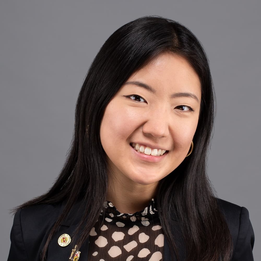 A professional headshot of Jessica Lee, who has Maryland-themed broaches on the lapel of their blazer.