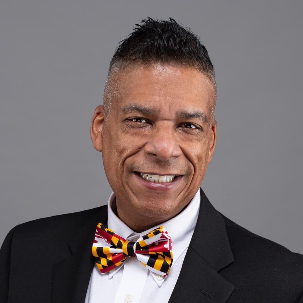 A professional headshot of Trevor Rickford wearing a Maryland-themed bowtie.