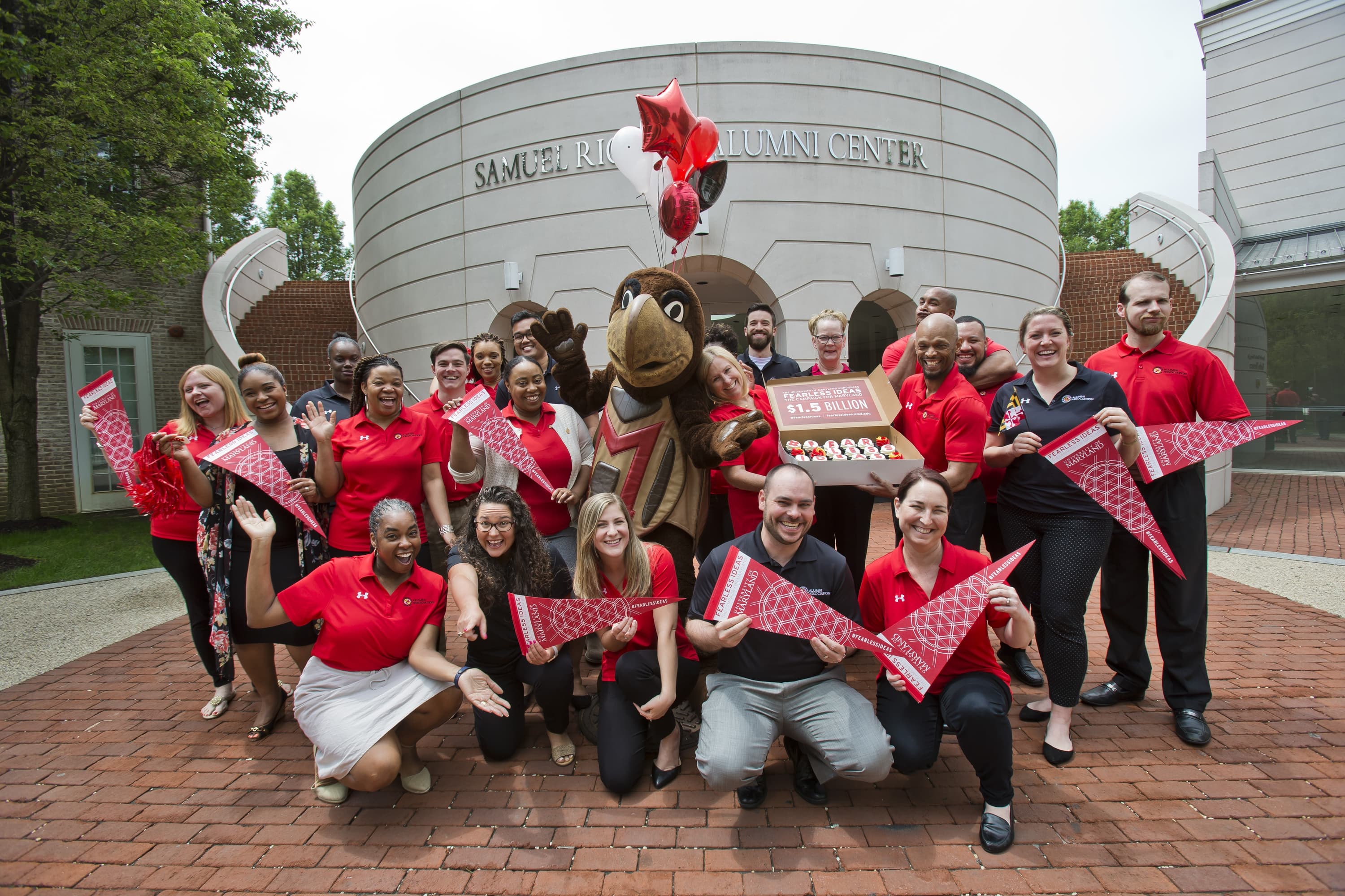 Members of the Alumni Association celebrate reaching the Fearless Ideas Campaign goal with a group photo and cupcates in front of the Riggs Alumni Center