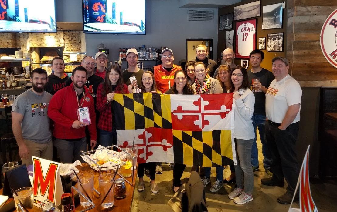 Group of alumni standing with a Maryland flag looking at the camera