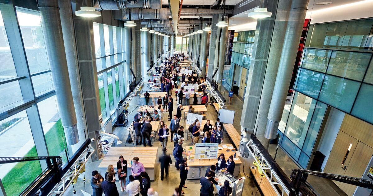 View looking down at a long room with clusters of people gathered around tables at the Leidos Innovation Lab Student Competition in A. James Clark Hall.