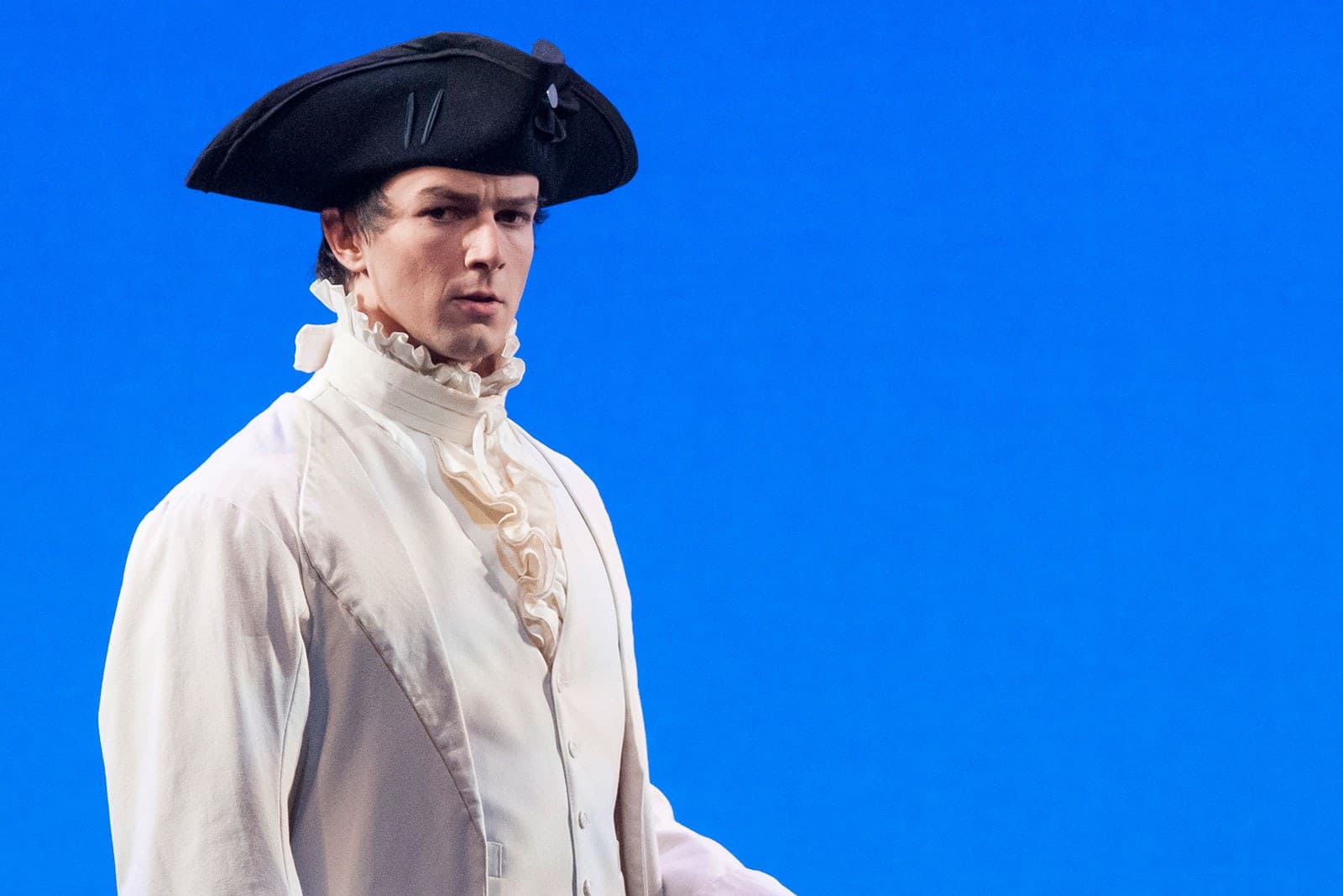 A man poses in a white frilly shirt and a pirate hat.