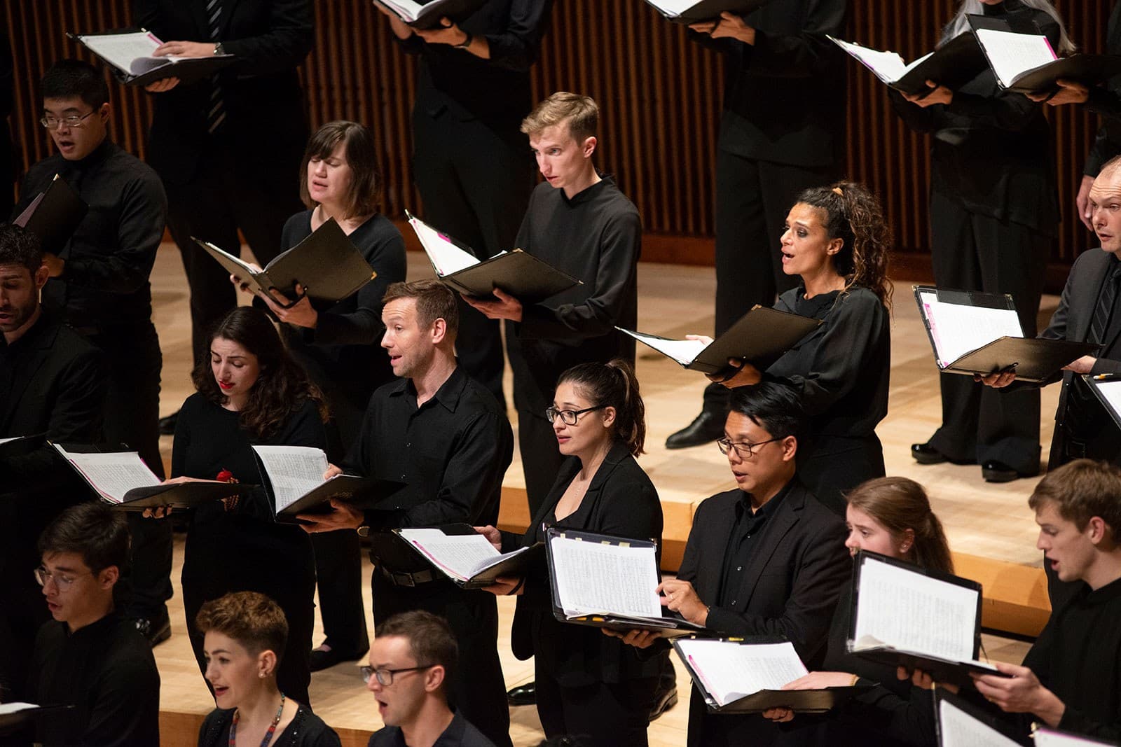 Choir members wearing black outfits hold folders as they perform on stage.