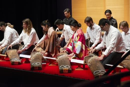 Men and women play traditional Japanese kotos on stage.