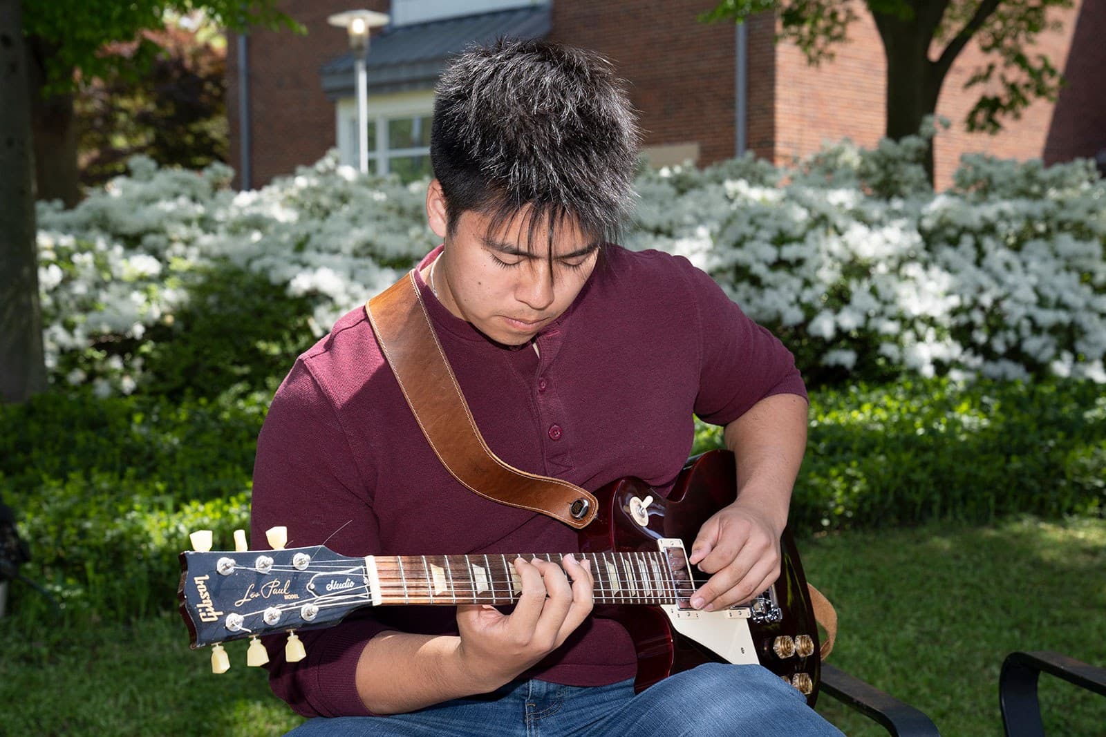 An asian male student plays electric guitar in a garden.