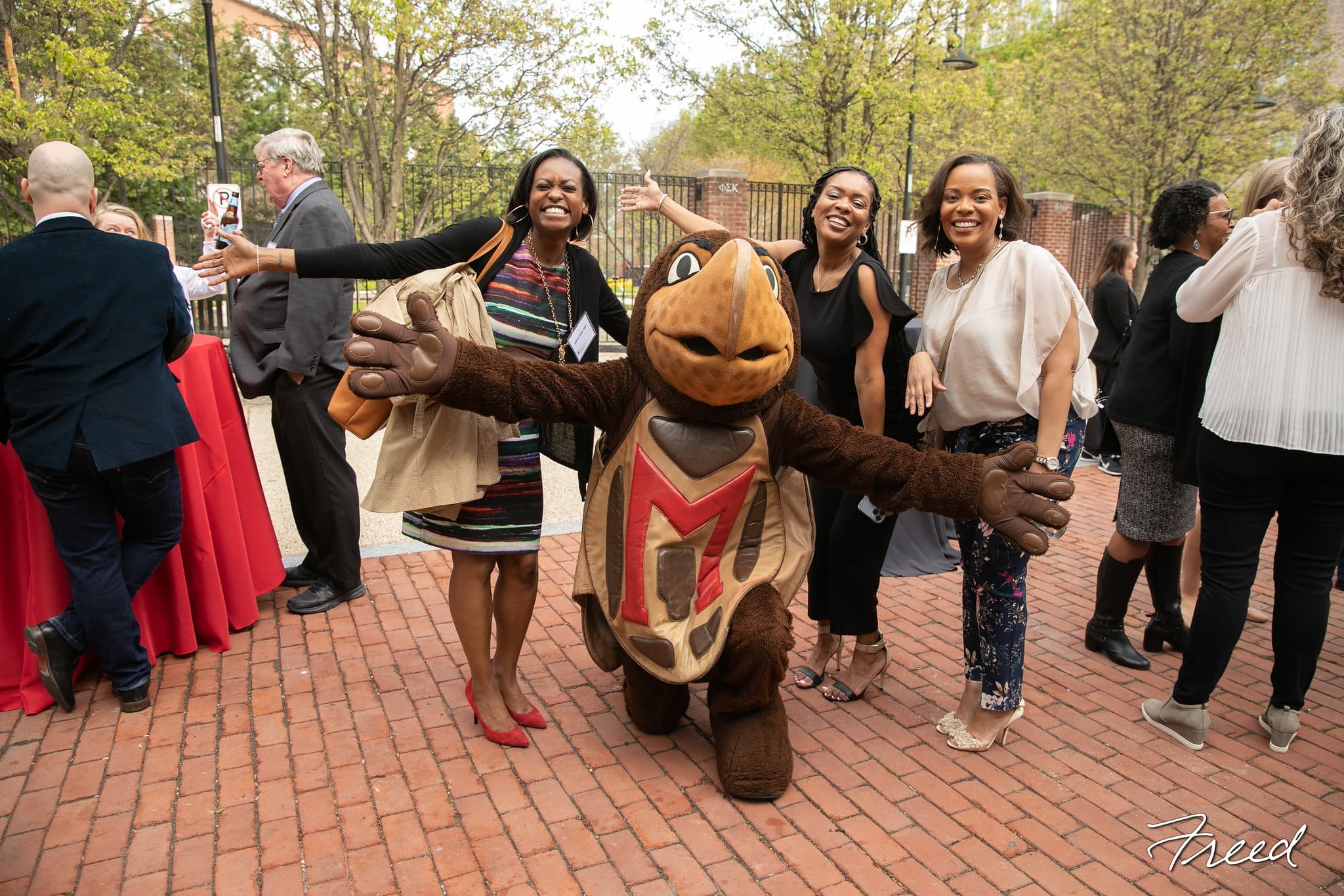 An image of three women standing and smiling with Testudo.