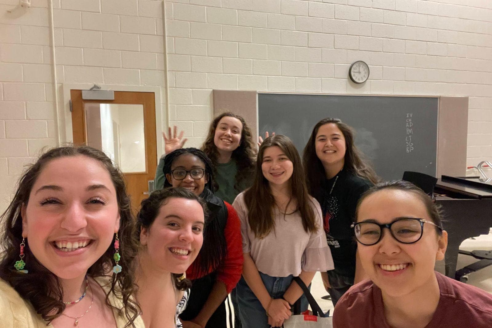 Seven women pose for a selfie in a music classroom.