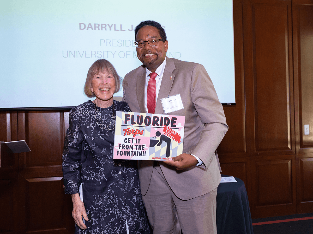 Dr. Alice Horowitz stands next to President pines, both smiling. They hold a sign together that reads "Fluoride: terps get it from the tap!"