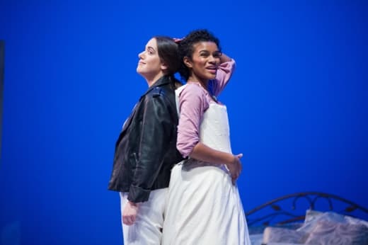 A black woman and white women pose back-to-back on stage.