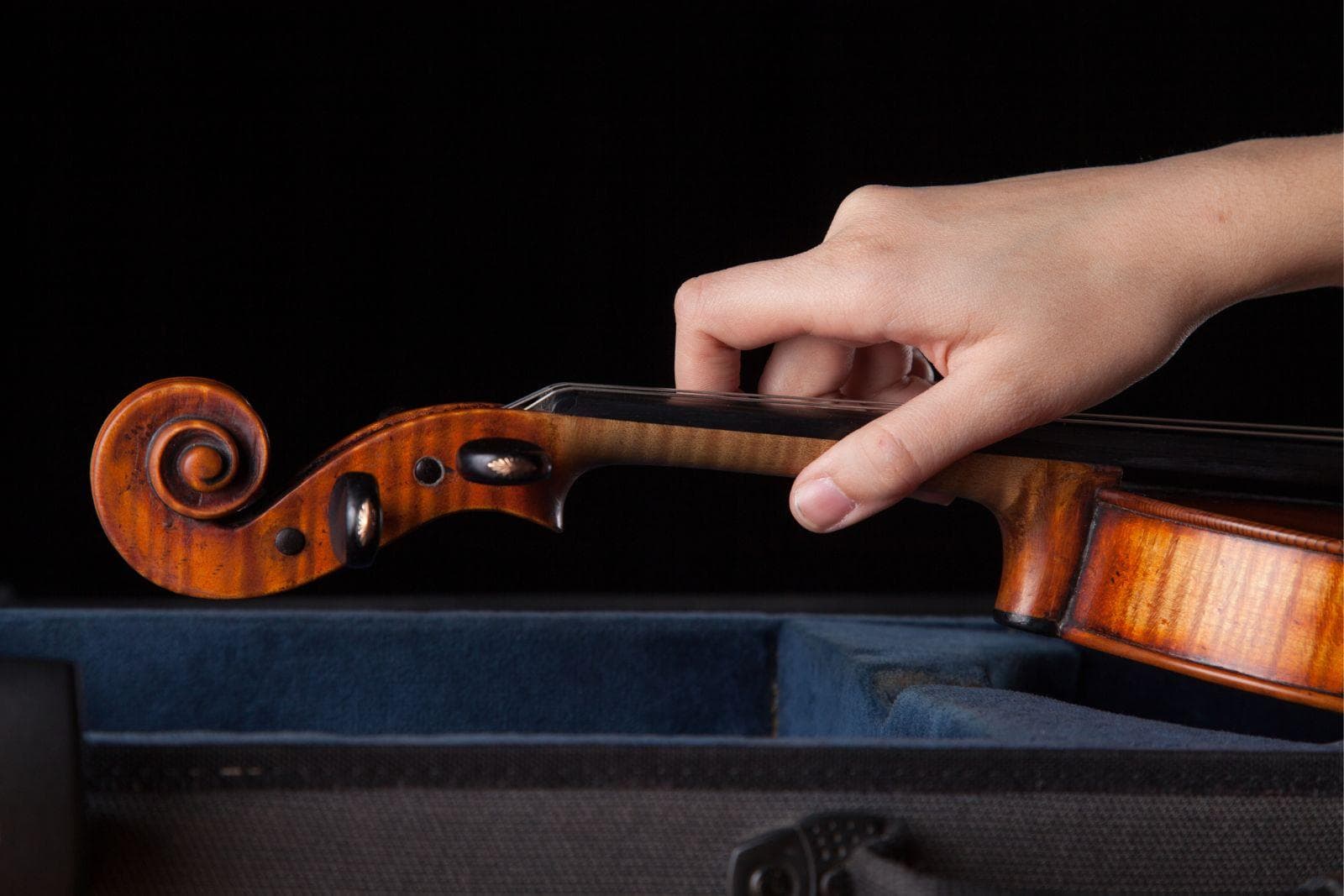 A hand reaches to pick up a violin.