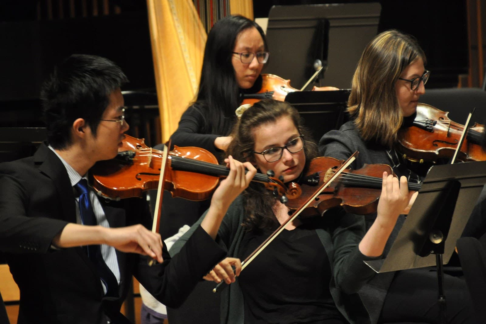 Four students play violins on stage.