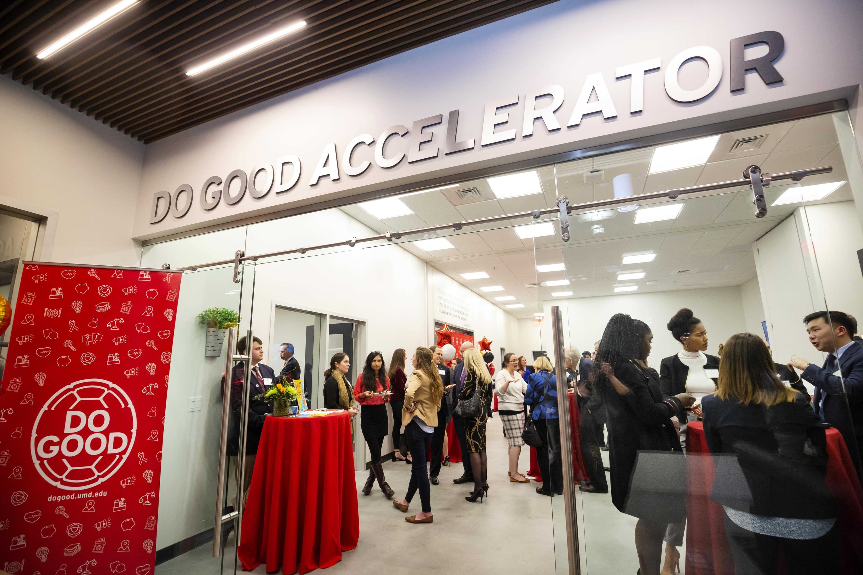 A large group of people are standing around cocktail tables and socializing in the Do Good Accelerator.