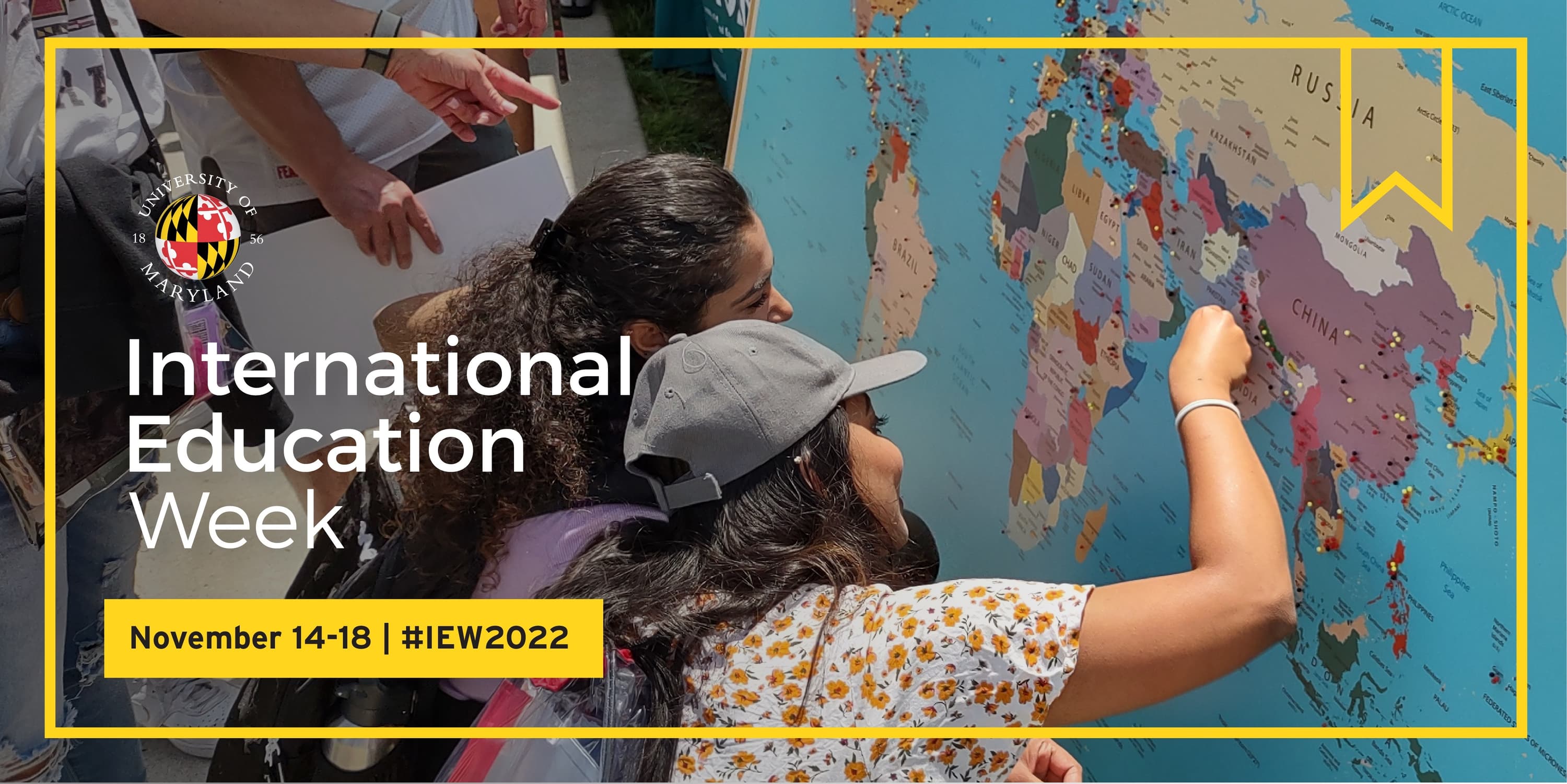 Two students place pins into a large map of the world. Overlaying text reads: International Education Week, November 14-18 #IEW2022