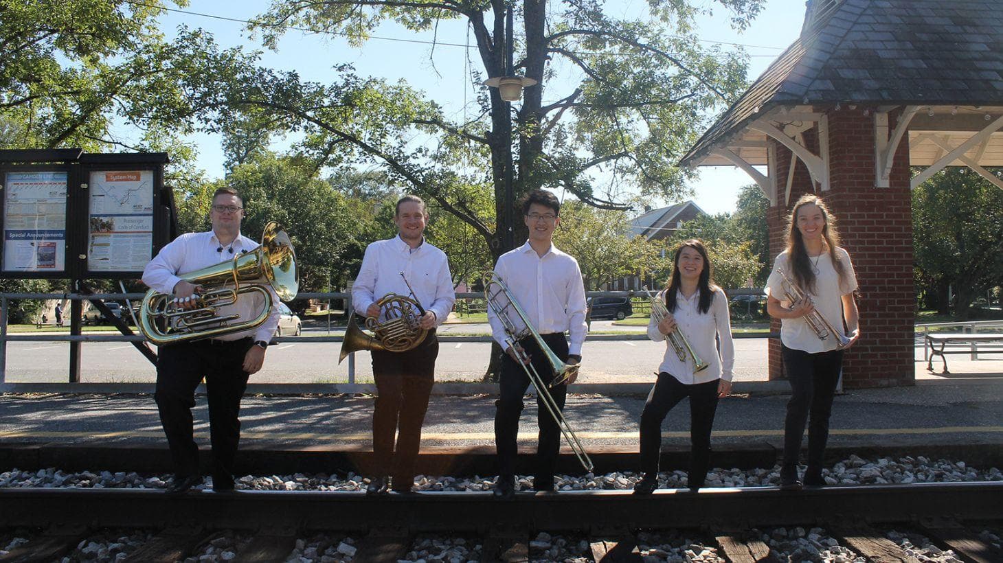 Members of the Terrapin Brass quintet pose with their instruments on train tracks.