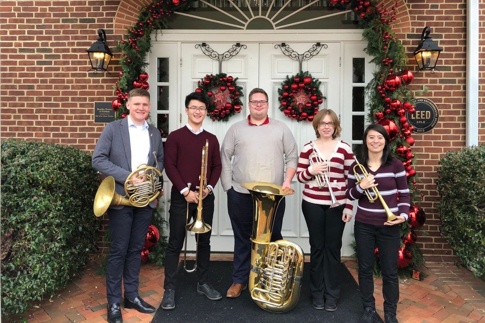 Four musicians pose for a picture outside with their brass instruments.