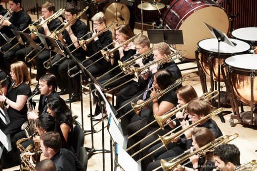 Student orchestra performs on stage with an array of wind instruments.