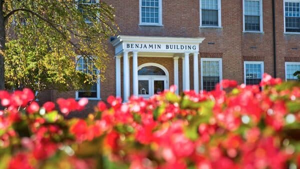 Front exterior of Benjamin Building, colorful red flowers out of focus in the foreground.