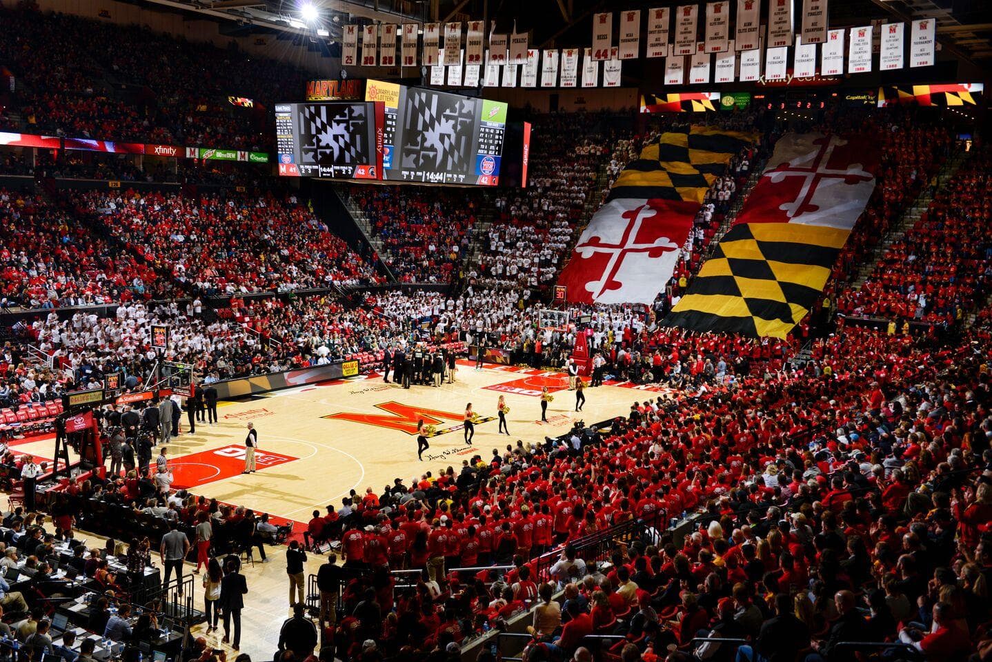 Overview of a men's basketball game with Maryland Flag unfurled over the fans and cheerleaders on the court.