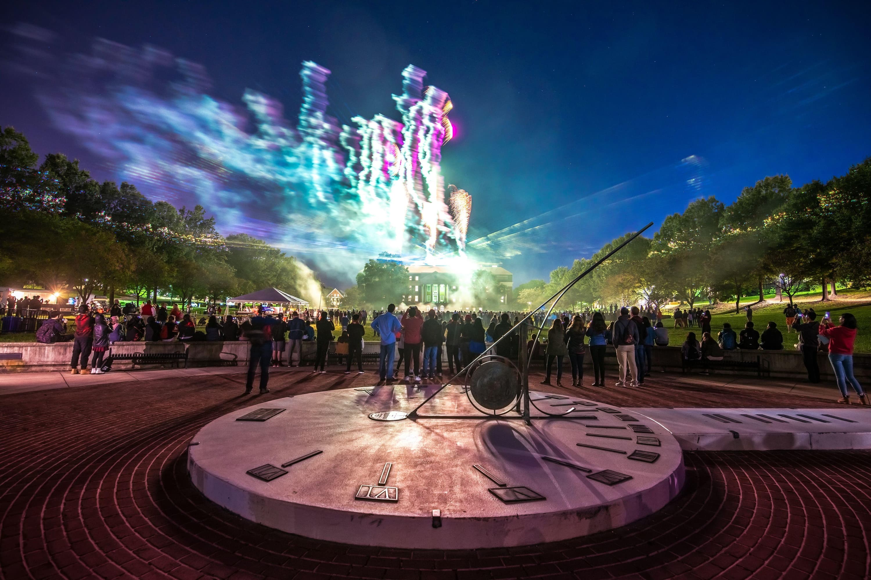 Photo of McKeldin Library at night with fireworks going off behind it, students stand in the foreground