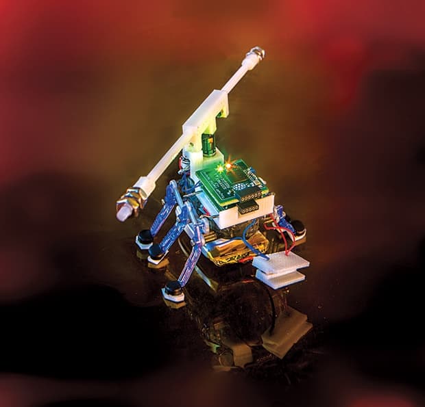 wires and light emitting diodes cover a very small six legged robot sitting on a shiny surface