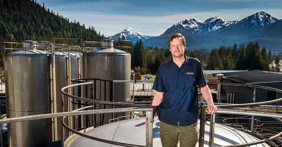 Geoff Larson ’80 poses near brewing equipment with mountains in the background