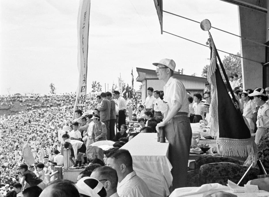 Toda standing looking out at outdoor stadium filled with youth.