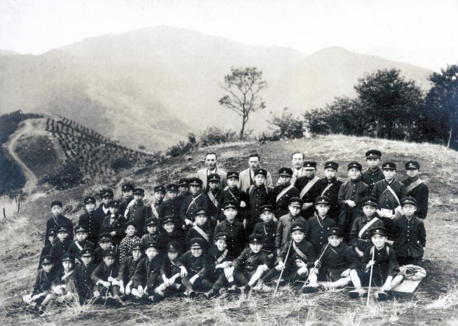 Group of school children posing for a group shot in front of a mountain landscape. Three teachers stand at the back center row.