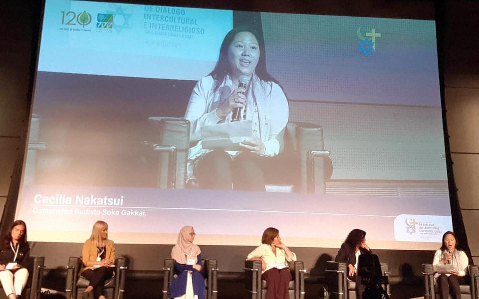 Six female panelists on stage with a backdrop of the person speaking.