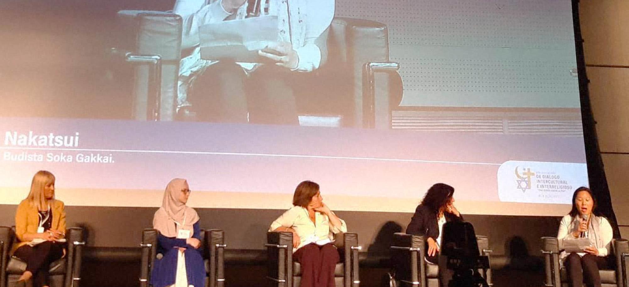 Six female panelists on stage with a backdrop of the person speaking.