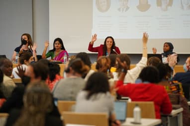 Four young women panelist with hands raised interact with audience