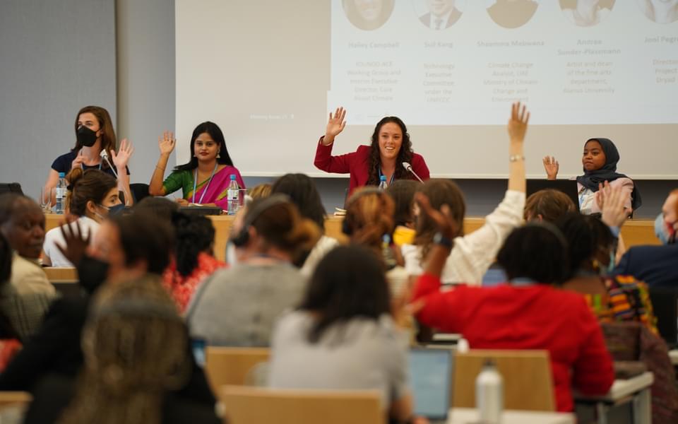 Four young women panelist with hands raised interact with audience