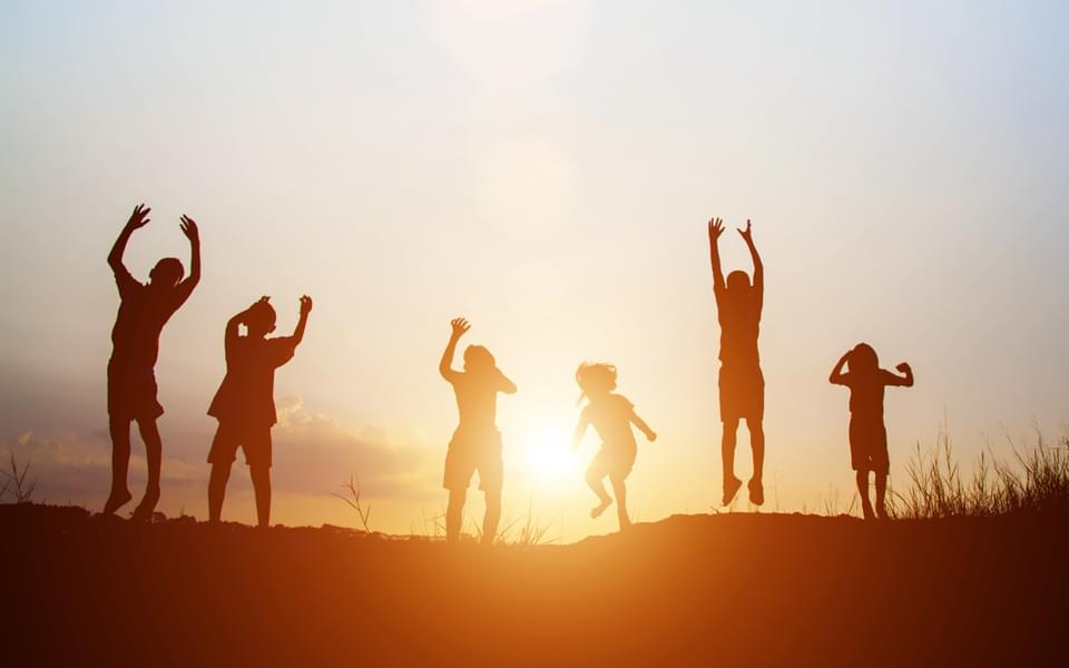 Silhouettes of six children playing outside hands joyfully raised in the air with sunset in background