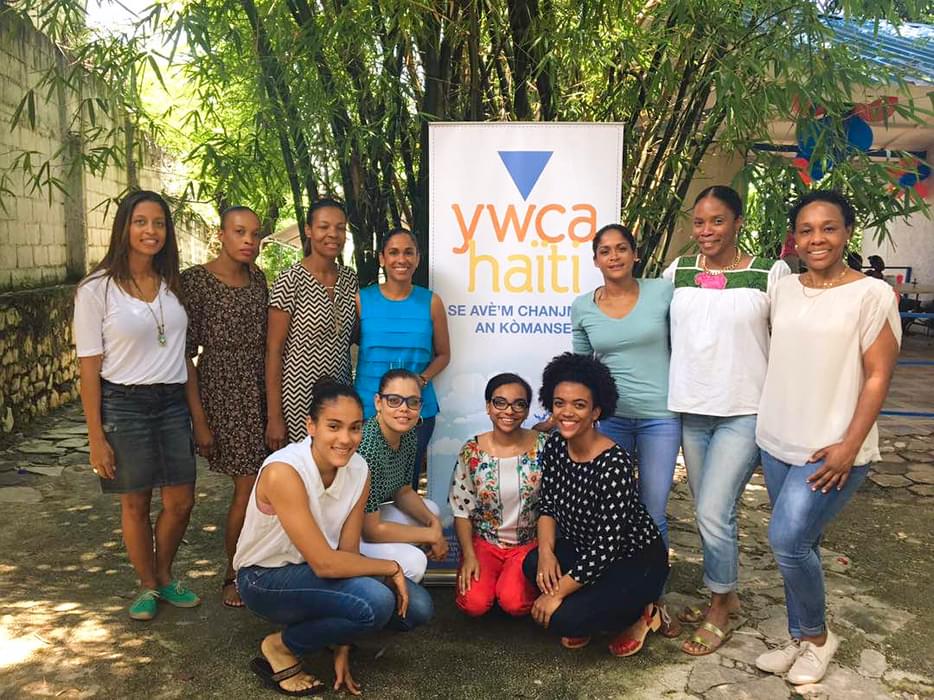 Adrianna in a group photo with young women in front of a YWCA Haiti sign