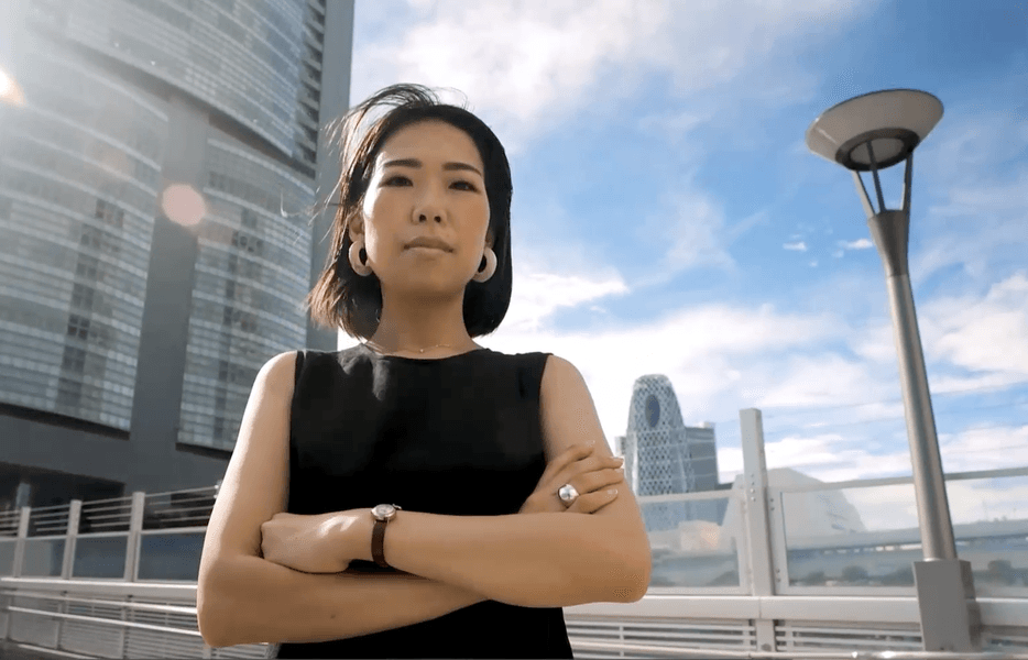 Young women with armed crossed looking directly at the camera with a cityscape in the background
