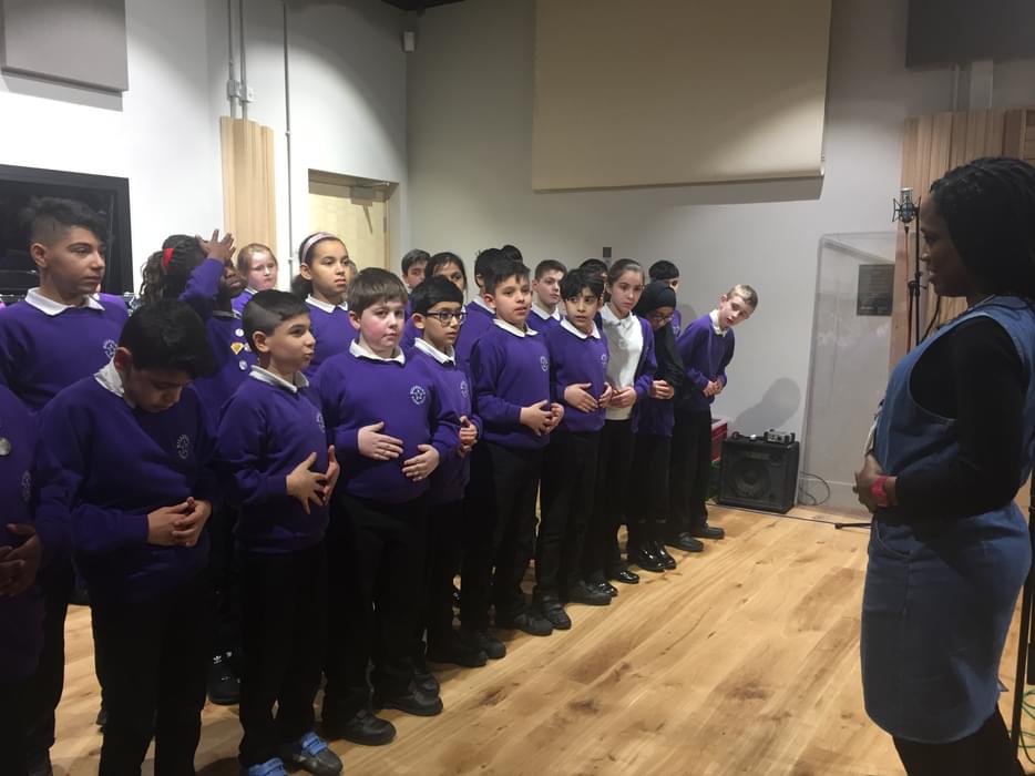 Bobbie in front of a group of children with their hands on their stomachs, during a singing lesson