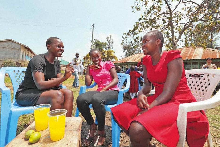 Three women seated smiling and talking. There are two glasses of juice on a table in front of them.