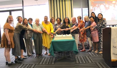 Group of diverse women with arms pointing toward celebratory cake