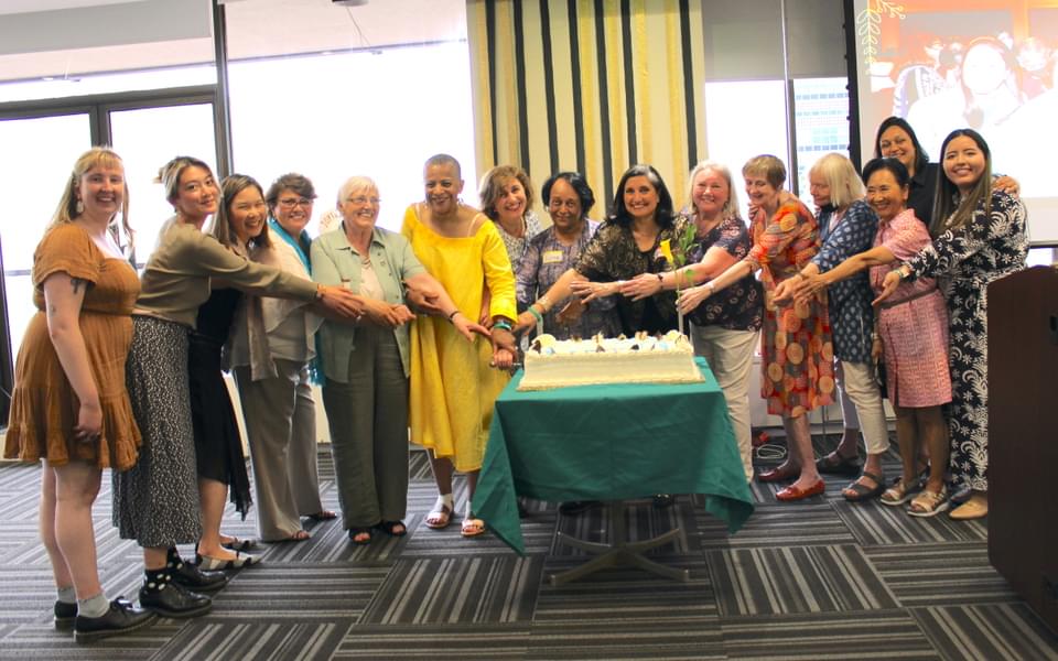 Group of diverse women with arms pointing toward celebratory cake